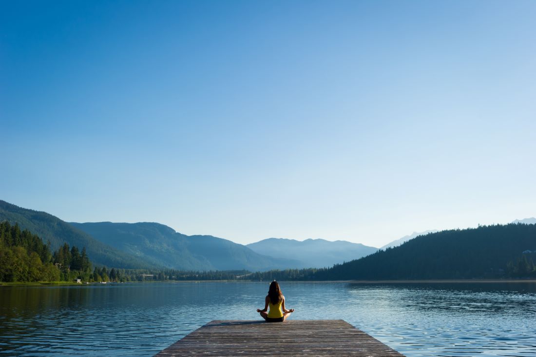 woman meditating on dock by water